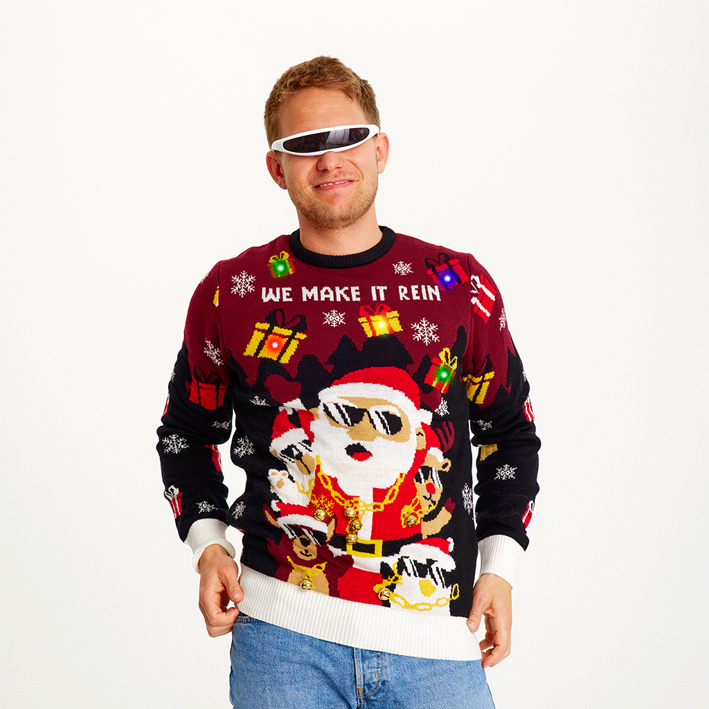 Un homme posant portant un pull de Noël rouge et noir avec le Père Noël et des lumières.